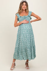 woman wearing a green floral maternity dress with ruffled sleeves and a tiered skirt, gently holding her baby bump