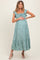 woman wearing a green floral maternity dress with ruffled sleeves and a tiered skirt, gently holding her baby bump