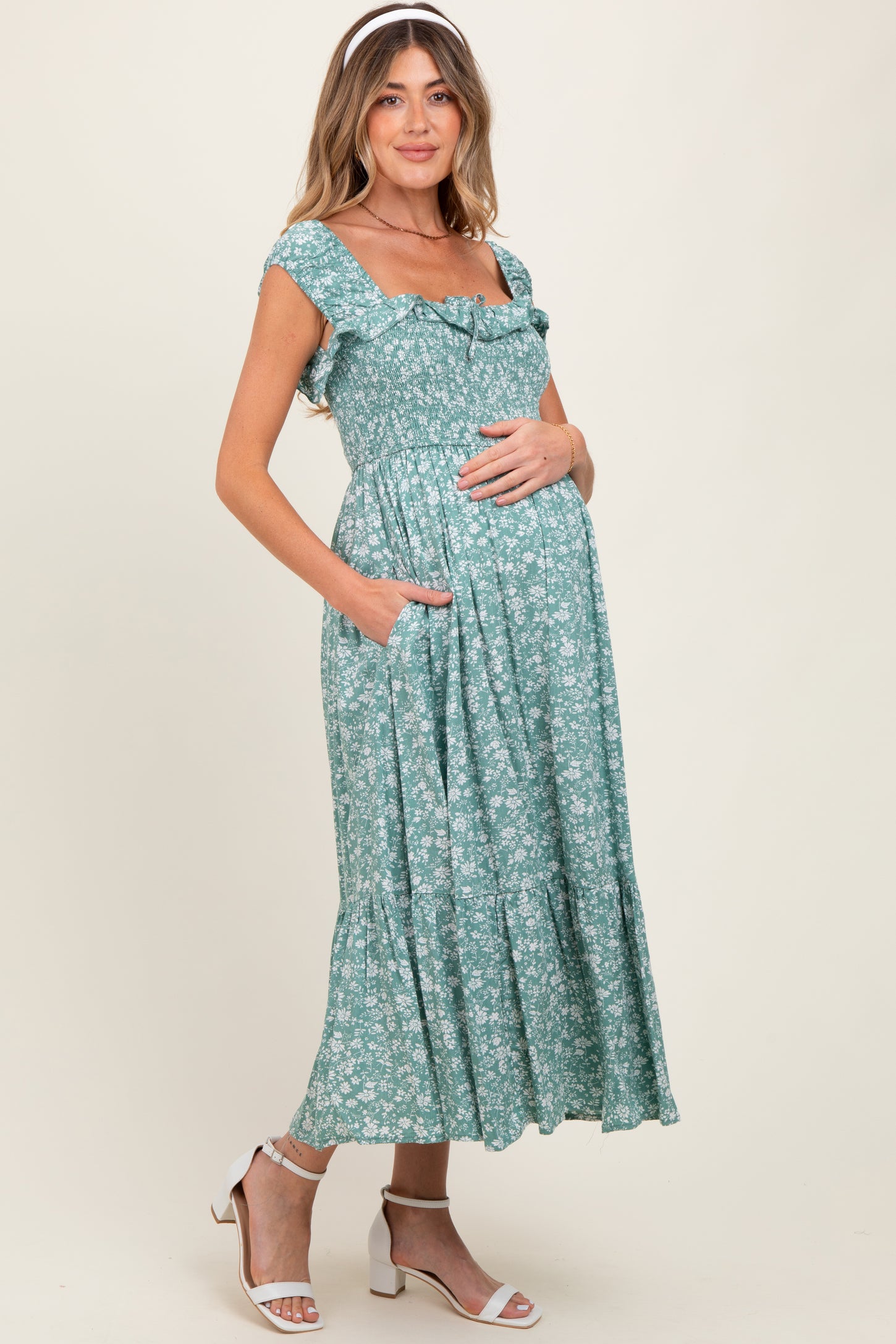 woman wearing a green floral maternity dress with a square neckline and pockets, showcasing her baby bump