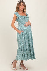 woman wearing a green floral maternity dress with a square neckline and pockets, showcasing her baby bump