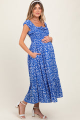woman wearing a blue floral maternity dress with short sleeves and pockets, holding her baby bump