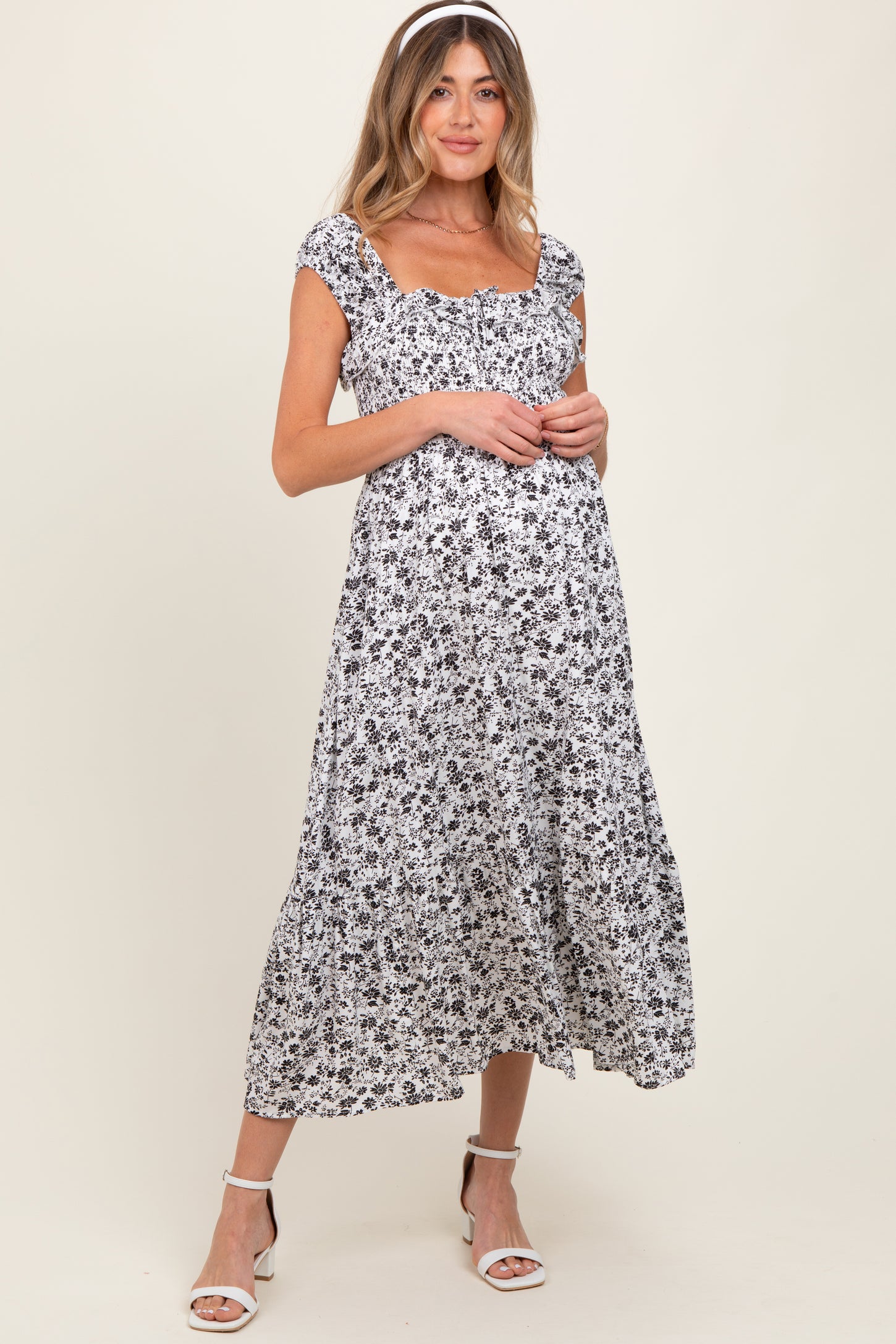 woman wearing a black and white floral maternity dress with a square neckline and flutter sleeves, showcasing her baby bump