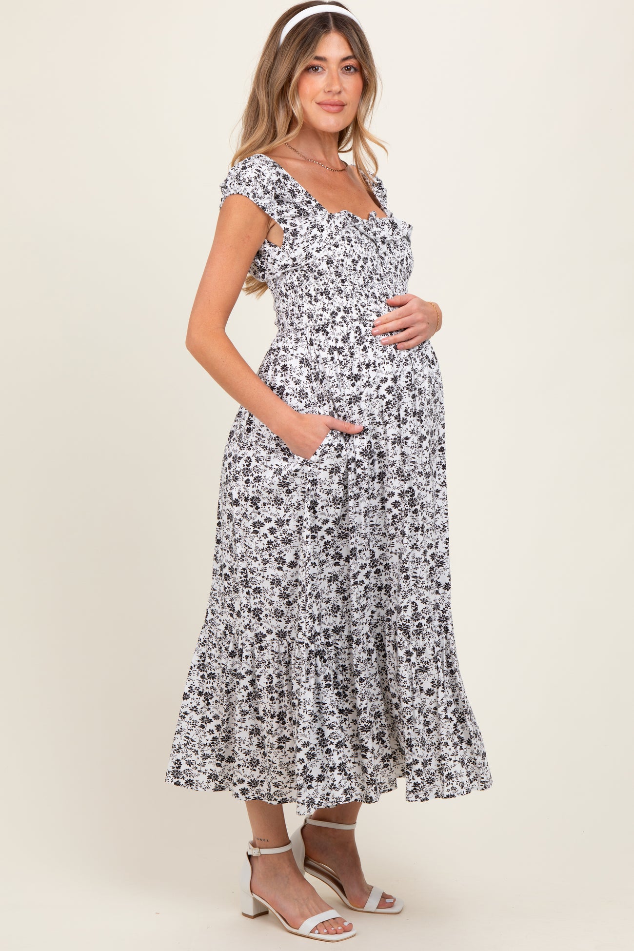 woman wearing a black and white floral print maternity maxi dress with pockets and holding her baby bump