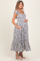 woman wearing a black and white floral print maternity maxi dress with pockets and holding her baby bump