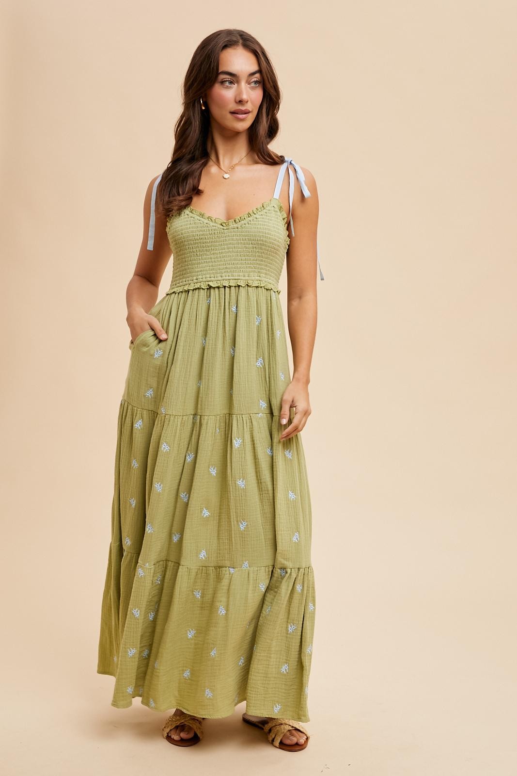 woman wearing a light green tiered maxi dress with blue embroidery and tie straps, featuring side pockets