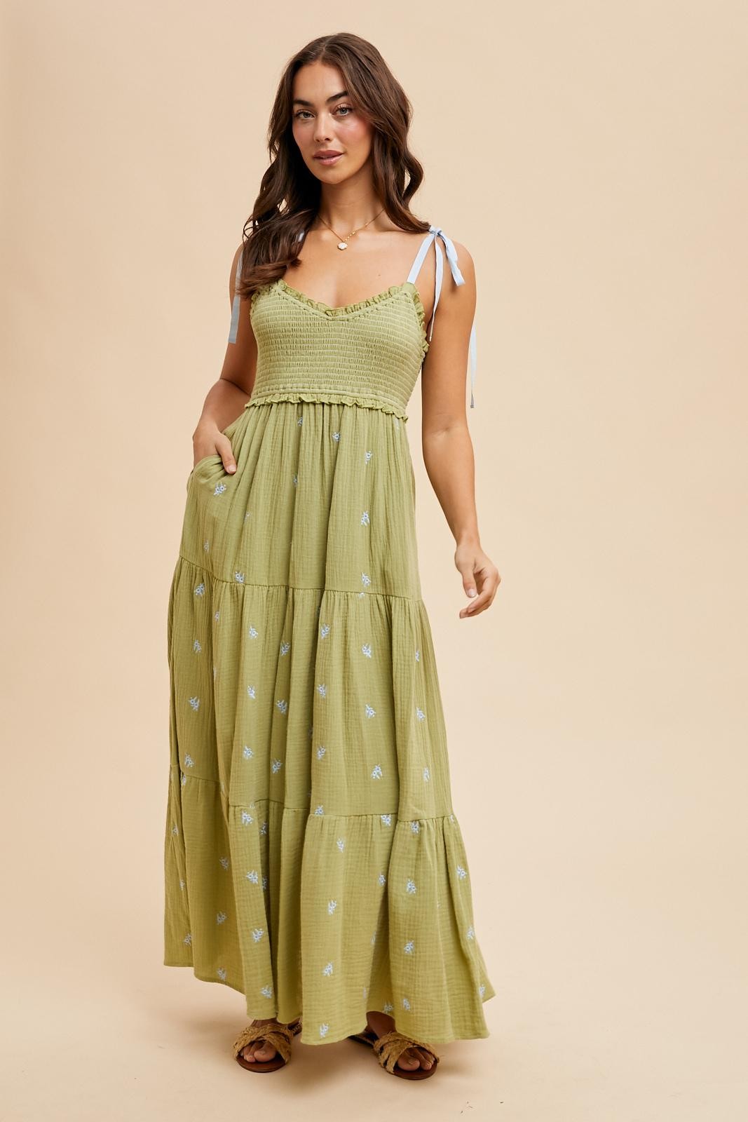 woman wearing a green tiered maxi dress with adjustable straps and floral embroidery details