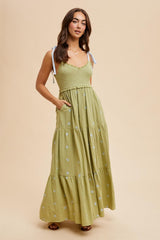woman wearing a light green maxi dress with embroidered details and adjustable shoulder straps, featuring pockets
