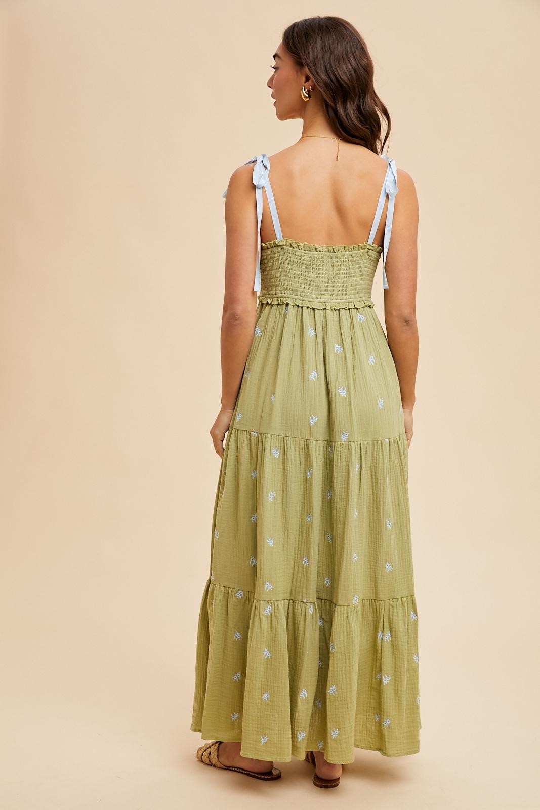 woman wearing a light green tiered maxi dress with embroidered details and blue tie straps, shown from the back