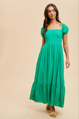 woman wearing a bright green maxi dress with puff sleeves and a square neckline, styled with golden sandals