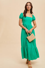 woman wearing a green puff sleeve maxi dress and holding a small woven handbag