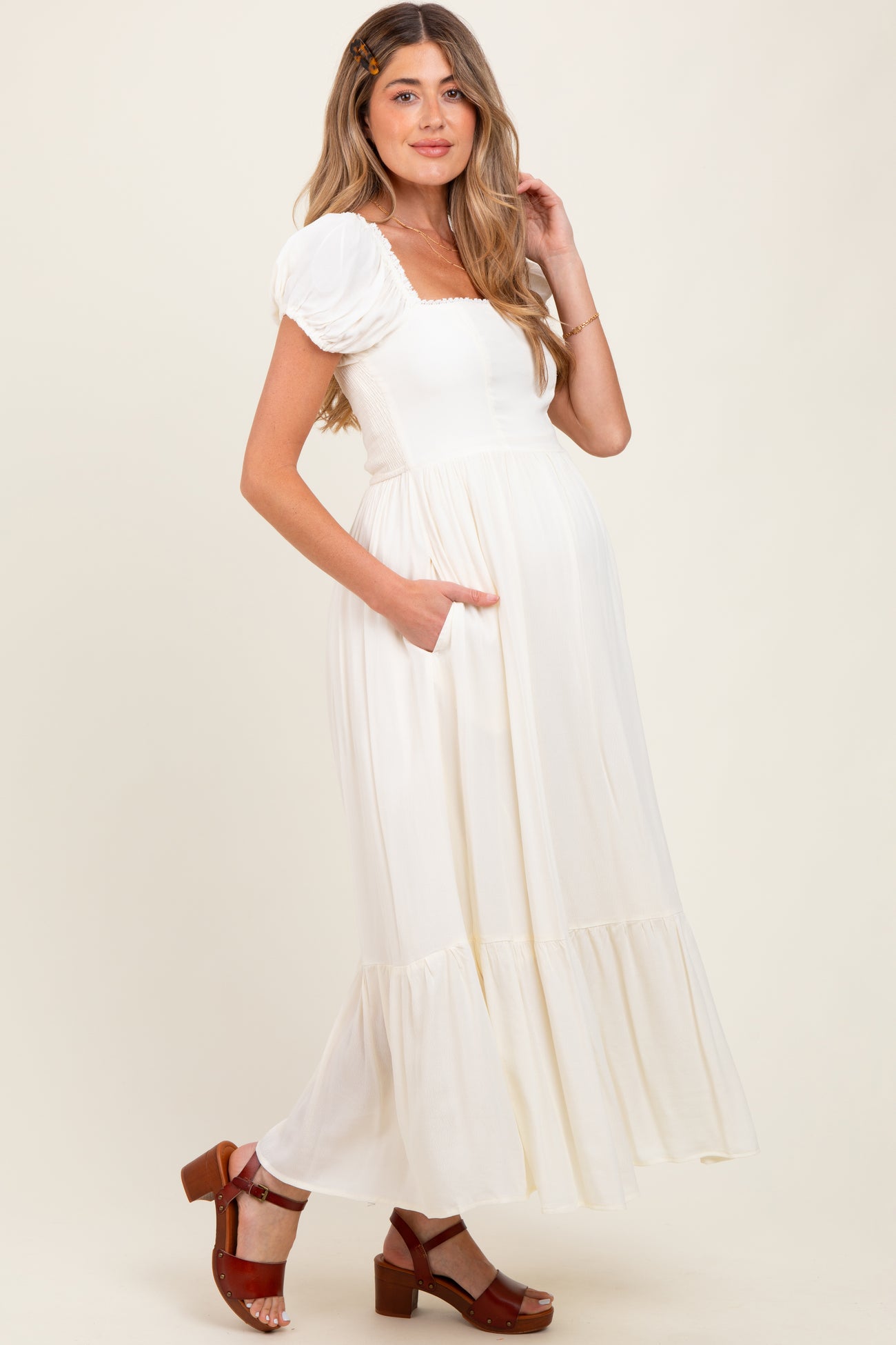 woman wearing a white puff sleeve maternity dress with pockets and a tiered hem, showing off her baby bump
