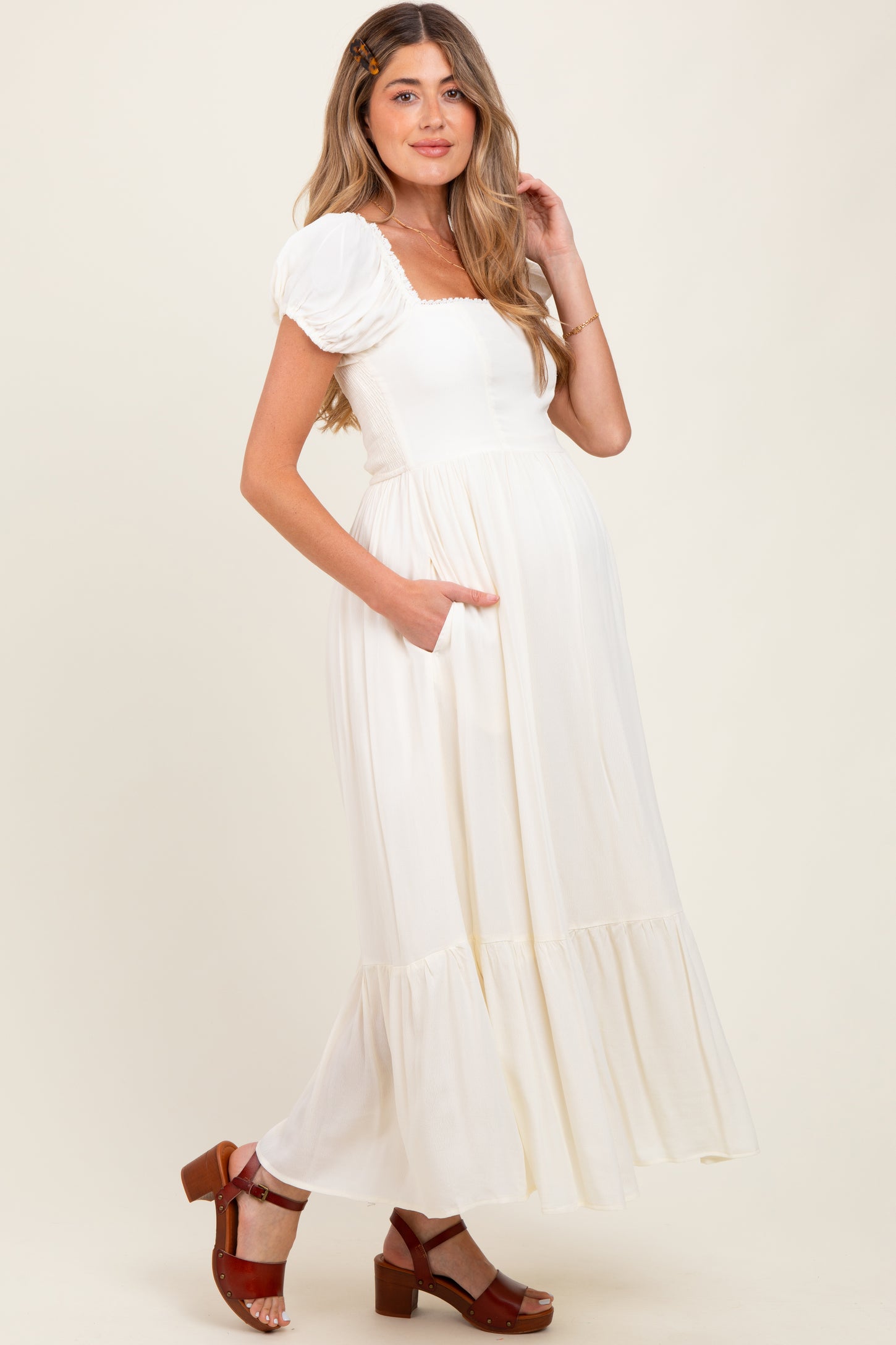 woman wearing a white puff sleeve maternity dress with pockets and a tiered hem, showing off her baby bump