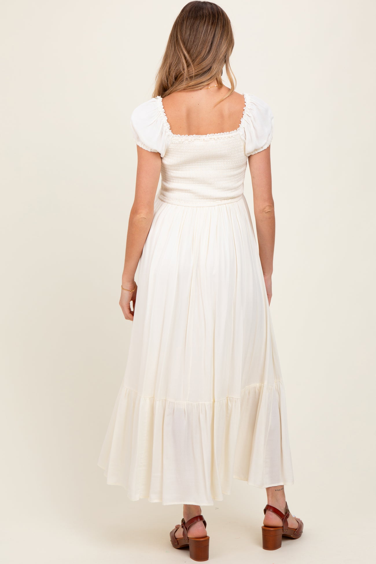 woman wearing a cream maternity maxi dress with puff sleeves and a smocked bodice, viewed from the back