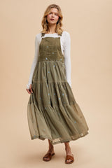 woman wearing an olive green tiered maxi dress with floral embroidery and a white long sleeve top, styled with sandals