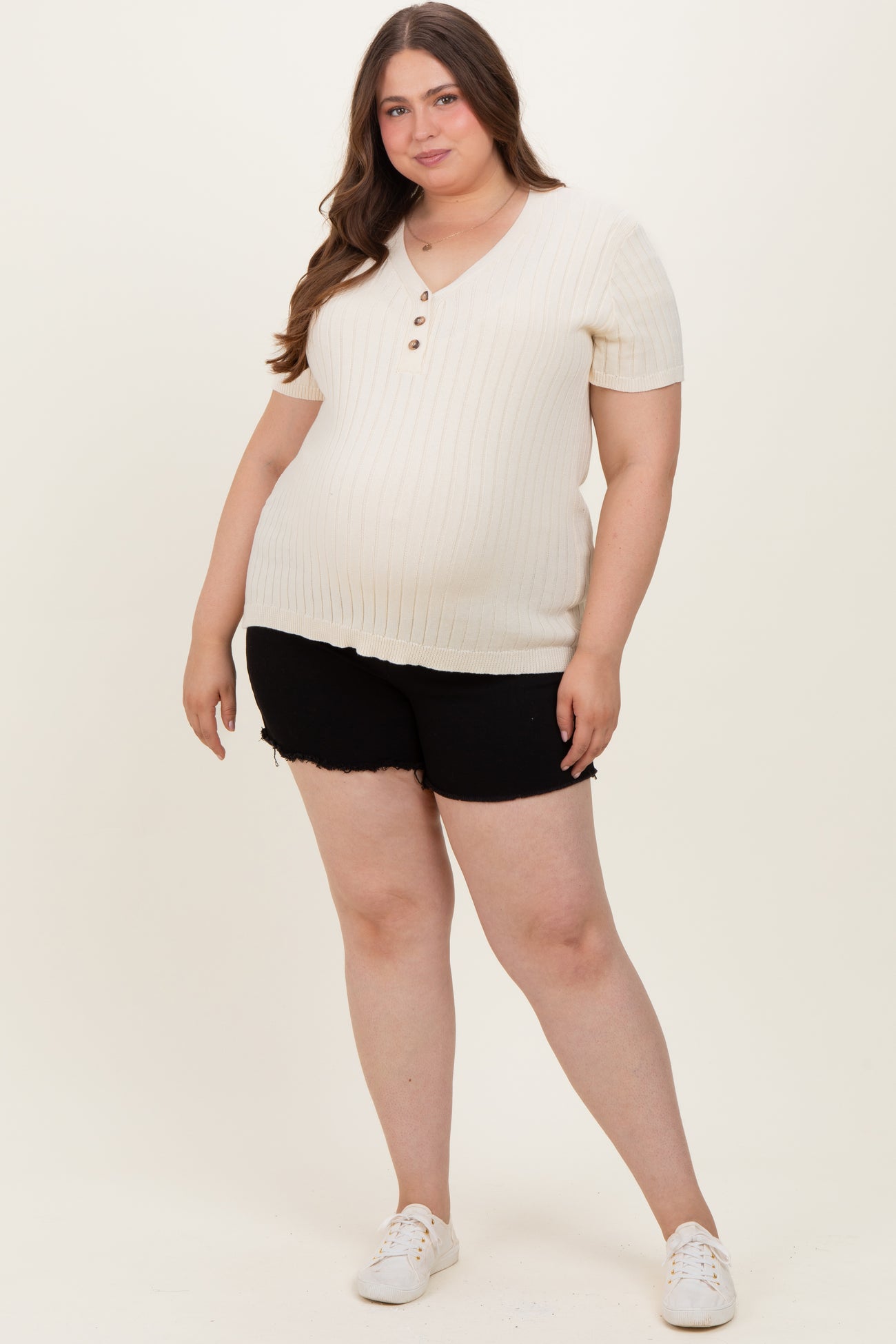 woman wearing a cream ribbed maternity top with a v-neck and buttons, paired with black shorts and showing her baby bump