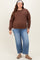 woman wearing a brown long sleeve maternity top and distressed blue jeans, showing a visible baby bump