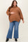woman wearing a brown oversized maternity sweater and blue flared maternity jeans, holding her baby bump
