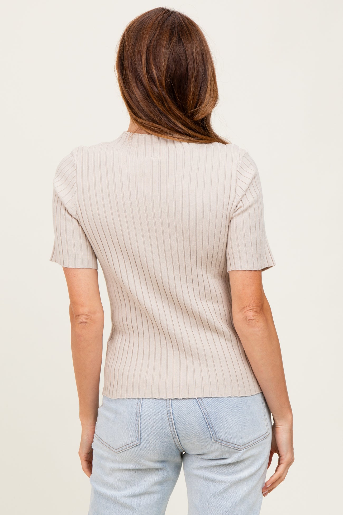 woman wearing a light beige ribbed short sleeve top, shown from the back with light blue high-waisted jeans