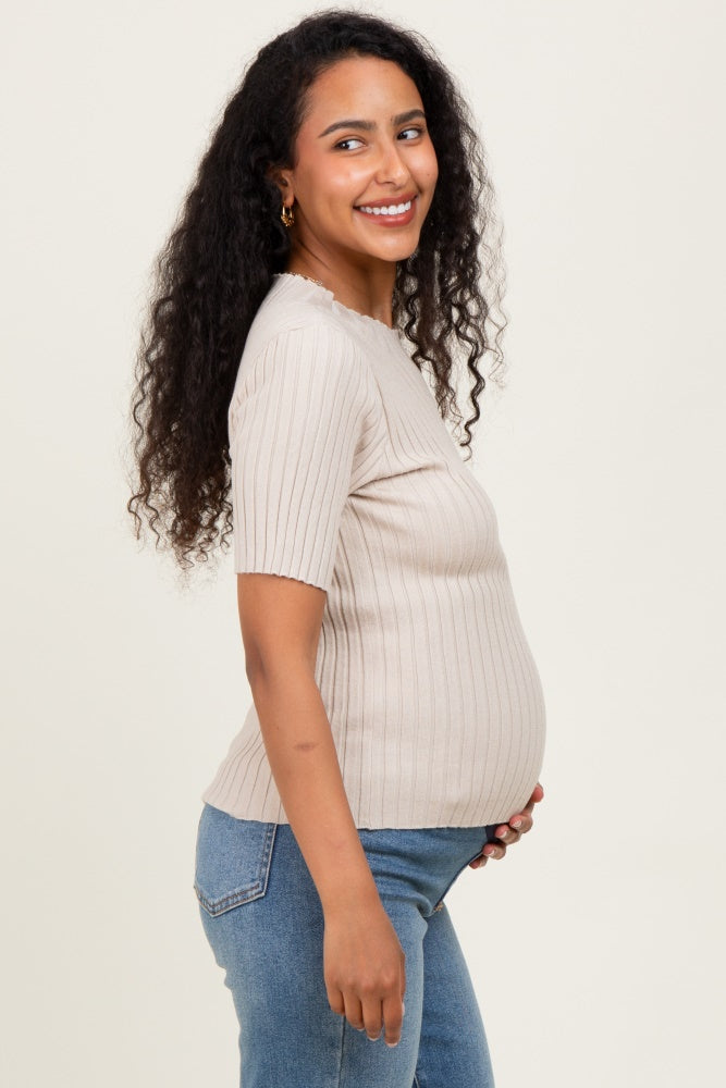 woman wearing a beige ribbed short sleeve maternity top and holding her baby bump