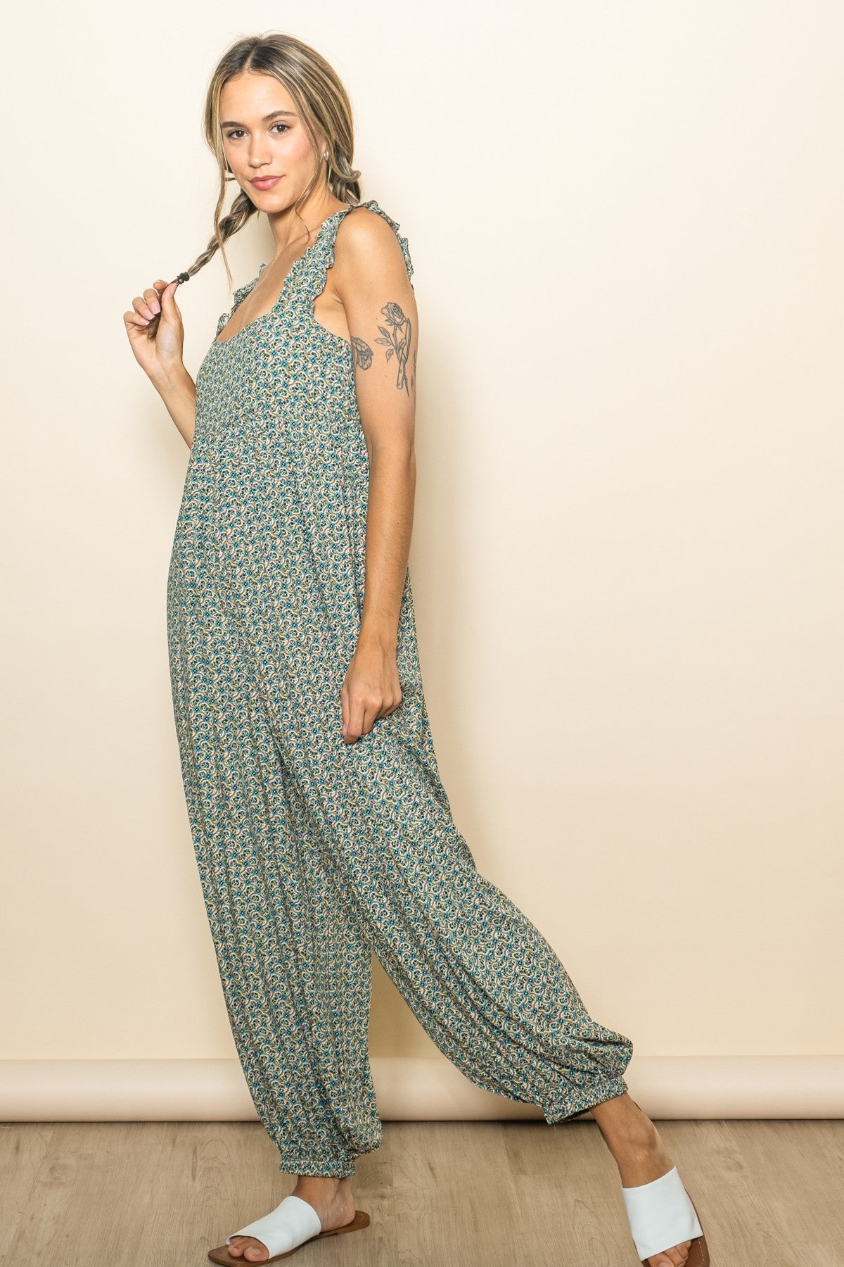 woman wearing a green floral jumpsuit with adjustable ties and loose fit, standing with braids in her hair