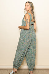 woman wearing a green floral jumpsuit with ruffled straps and an open back, standing sideways