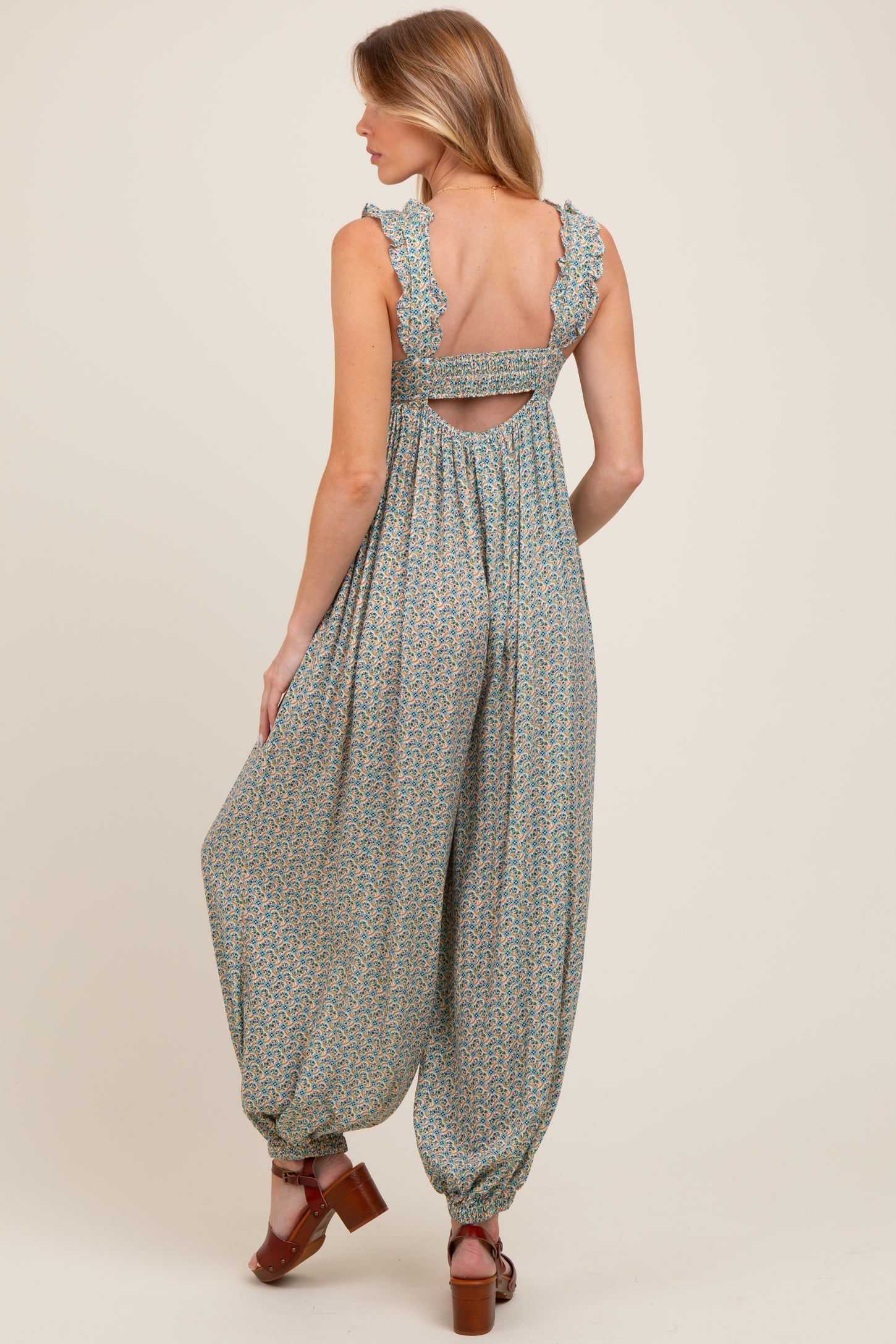 woman wearing a green floral patterned maternity jumpsuit with ruffled straps and an open back