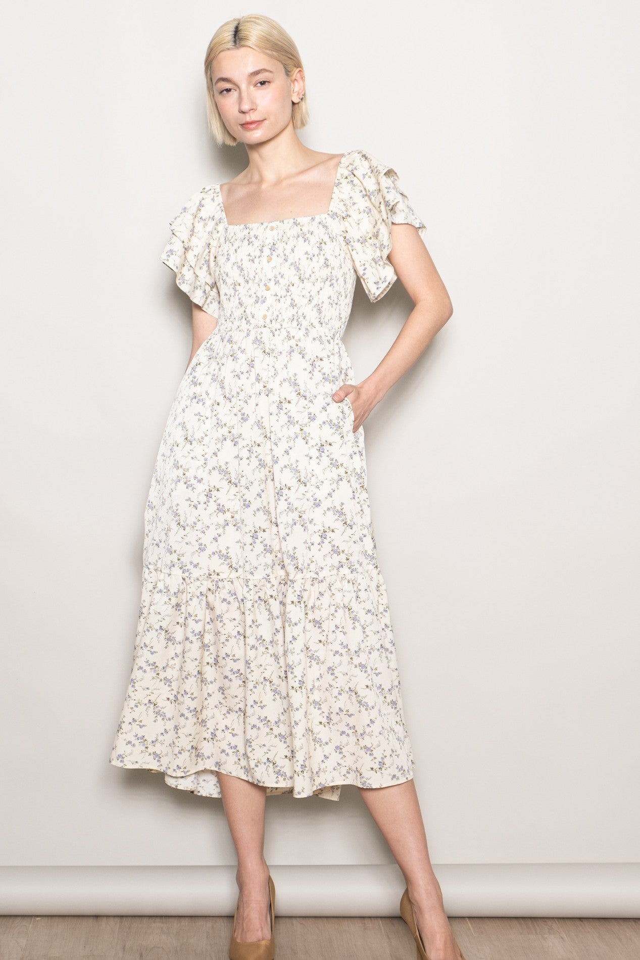 woman wearing a cream floral midi dress with ruffled sleeves and pockets, styled with nude heels