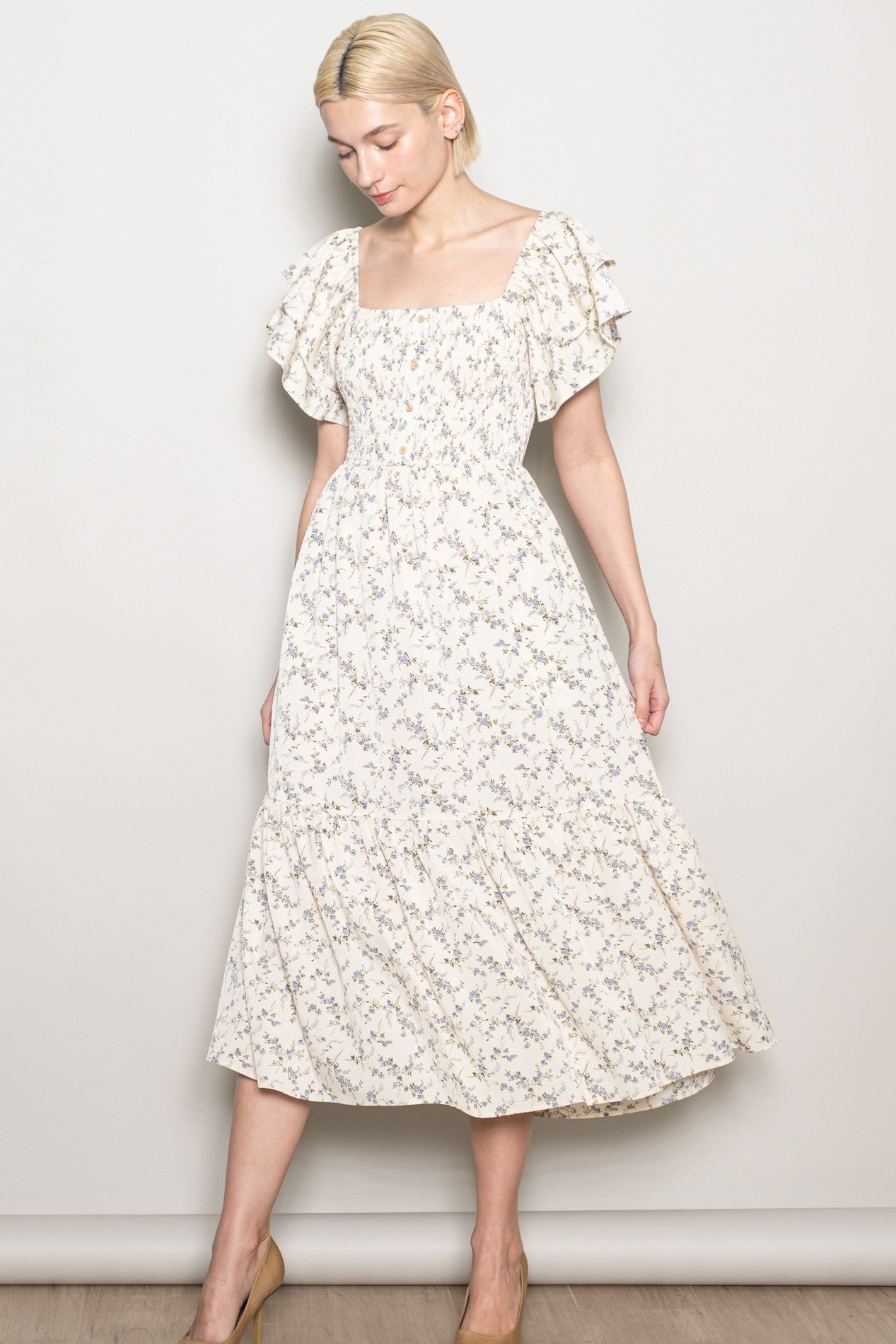 woman wearing a cream floral midi dress with ruffled sleeves and a square neckline, posing against a plain background
