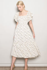 woman wearing a cream floral midi dress with ruffled sleeves and a square neckline, posing against a plain background