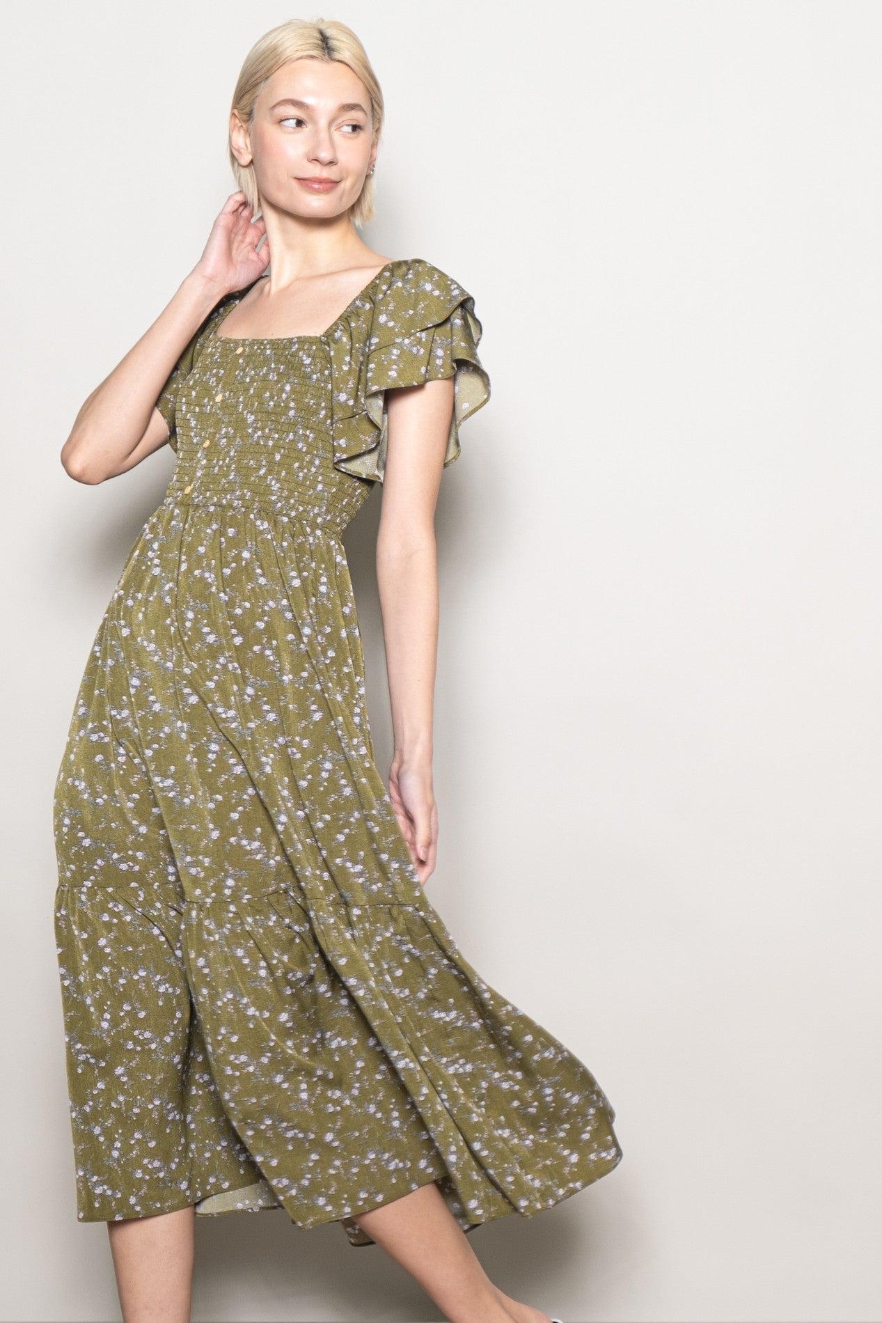 woman wearing an olive green floral midi dress with flutter sleeves and a smocked bodice