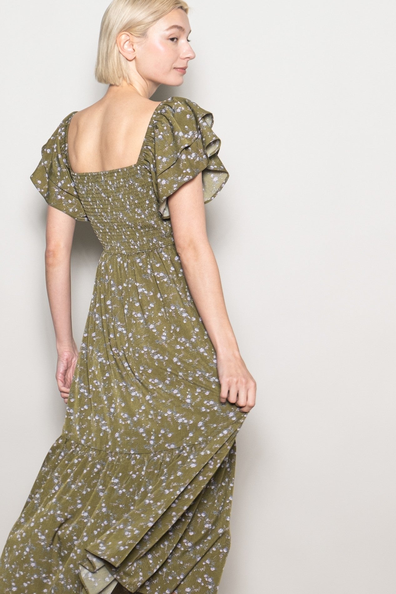 woman wearing an olive green floral maxi dress with puff sleeves and a smocked back, turning to the side