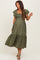 woman wearing a green floral print maternity dress with ruffled sleeves and a tiered skirt, holding one hand playfully