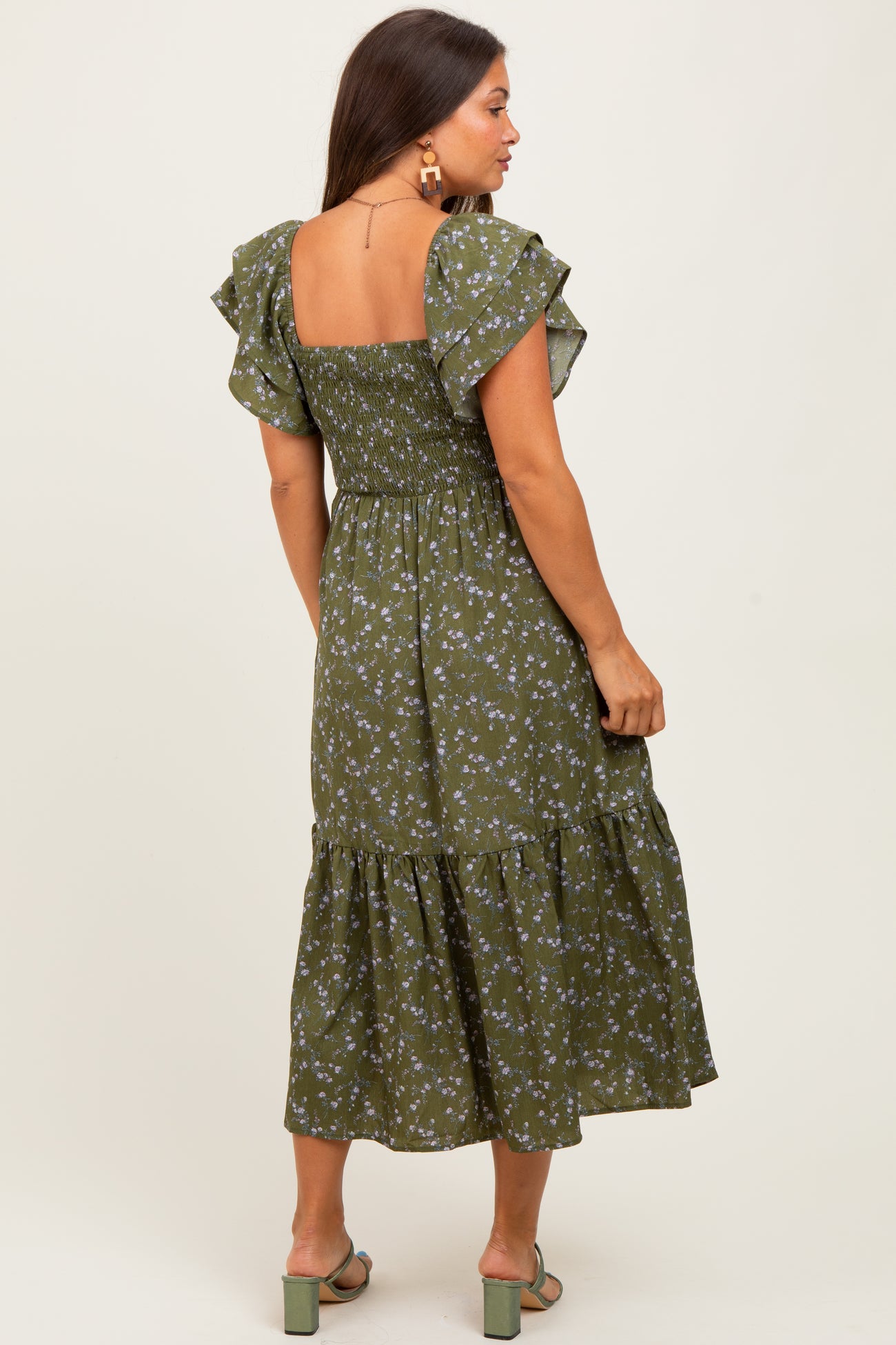 woman wearing a green floral maternity dress with ruffled sleeves and a tiered skirt, showing her baby bump from the back