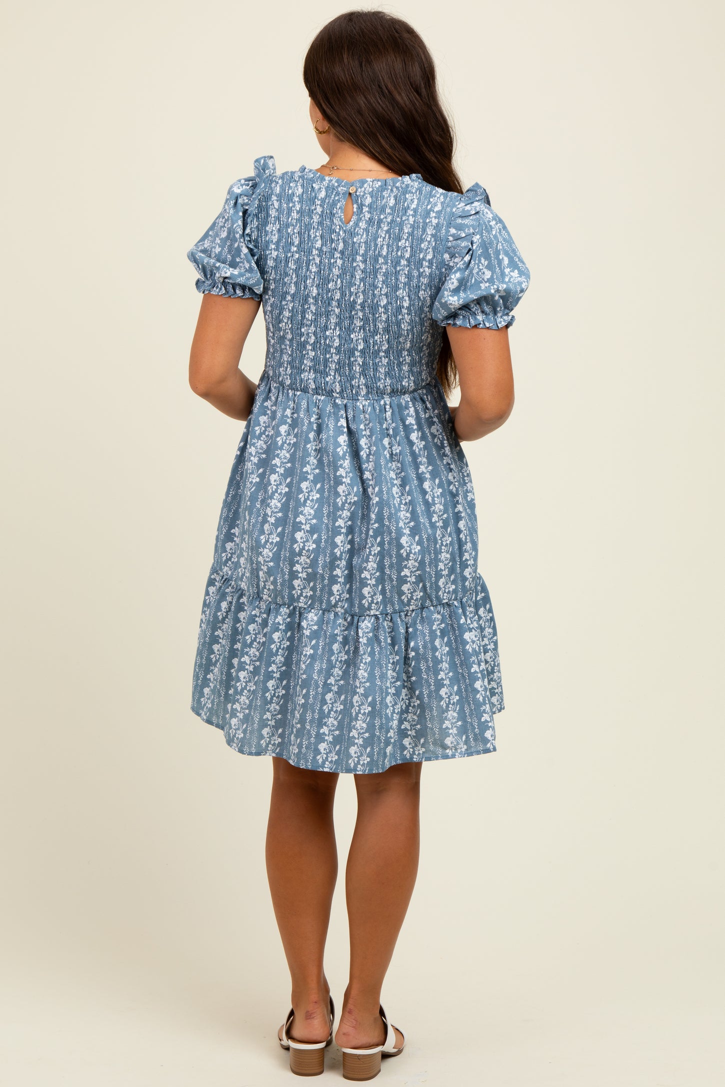 woman wearing a blue floral print maternity dress with puff sleeves and tiered skirt, showing a stylish back view