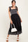 woman wearing a black elastic waist maxi dress with tie straps and embroidered hem, holding a white handbag