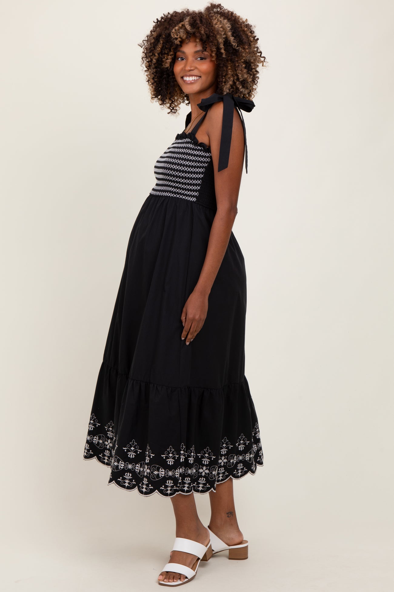 woman wearing a black maternity dress with embroidered details and a tiered hem, showing her baby bump