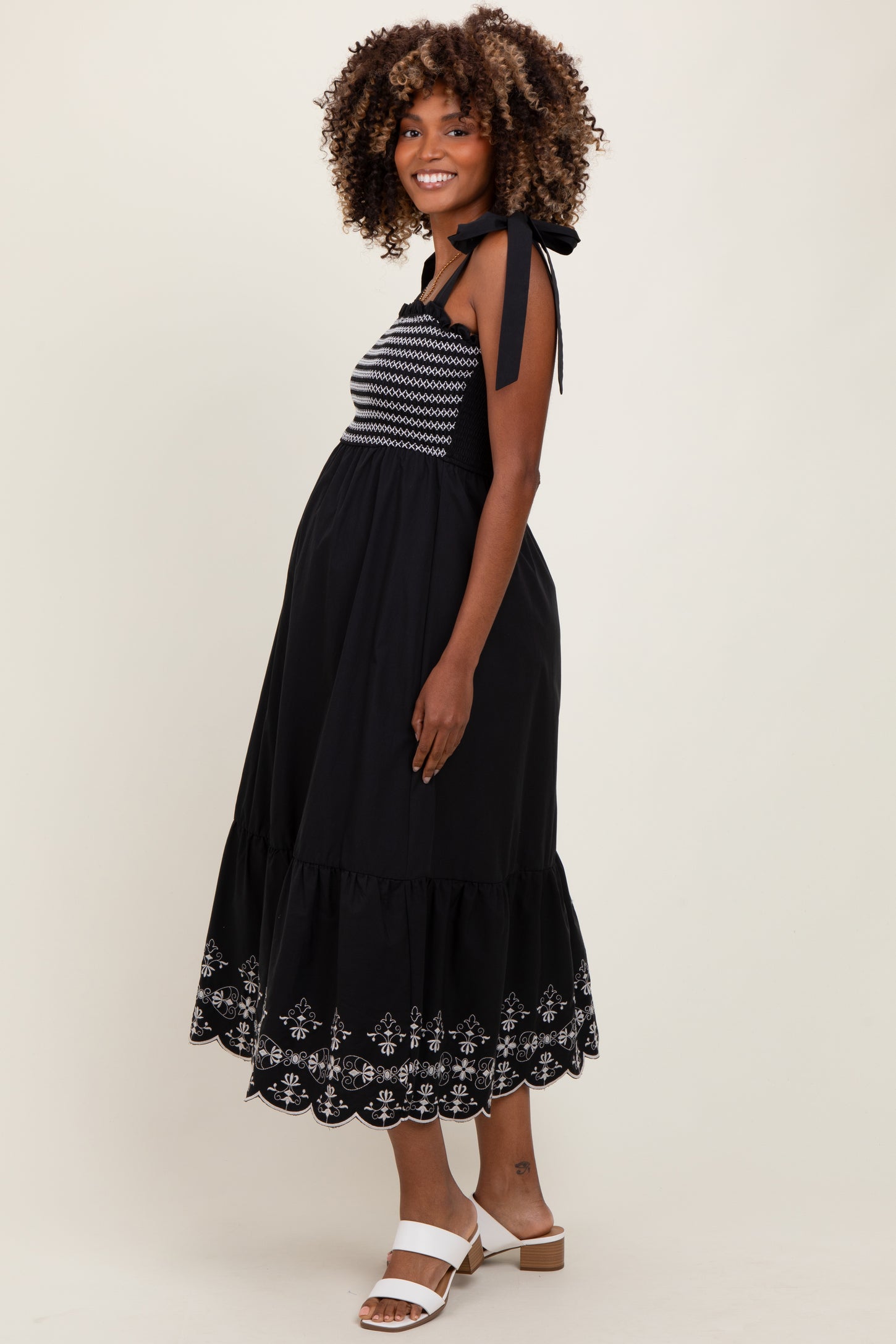 woman wearing a black maternity dress with embroidered details and a tiered hem, showing her baby bump