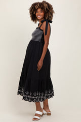 woman wearing a black maternity dress with embroidered details and a tiered hem, showing her baby bump