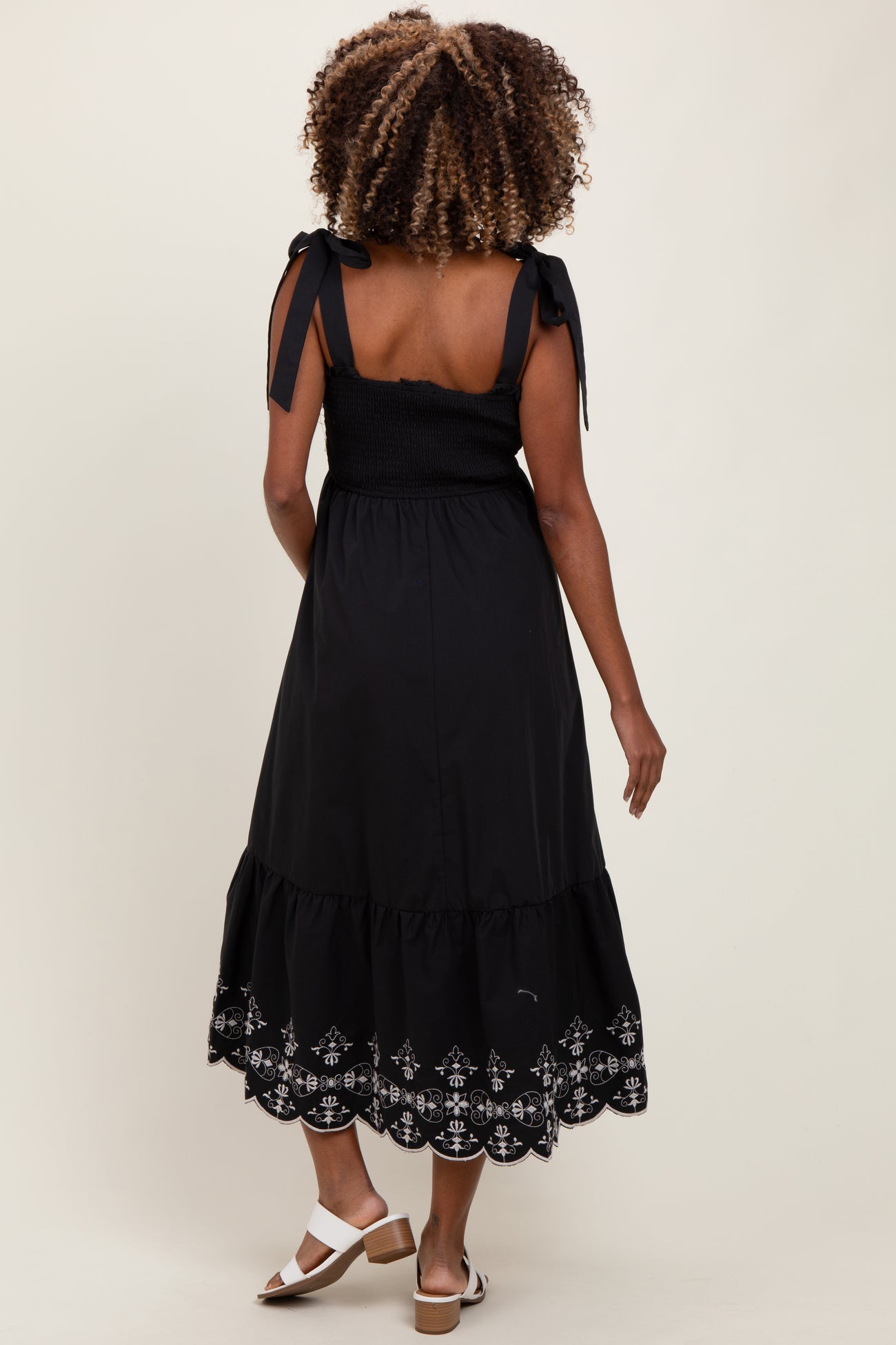 woman wearing a black maternity dress with tie straps and embroidered hem, showcasing a baby bump