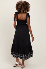 woman wearing a black maternity dress with tie straps and embroidered hem, showcasing a baby bump