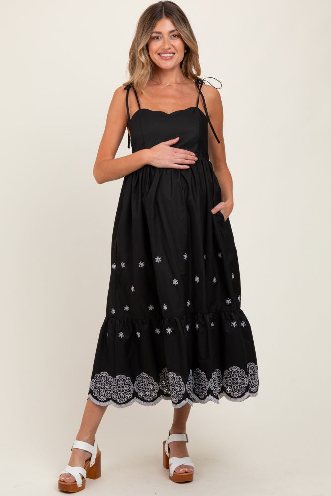 woman wearing a black maternity dress with adjustable straps, embroidered details, and a baby bump visible