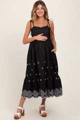 woman wearing a black maternity dress with adjustable straps, embroidered details, and a baby bump visible