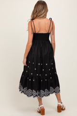 woman wearing a black maternity dress with embroidered details and spaghetti straps, showcasing a baby bump