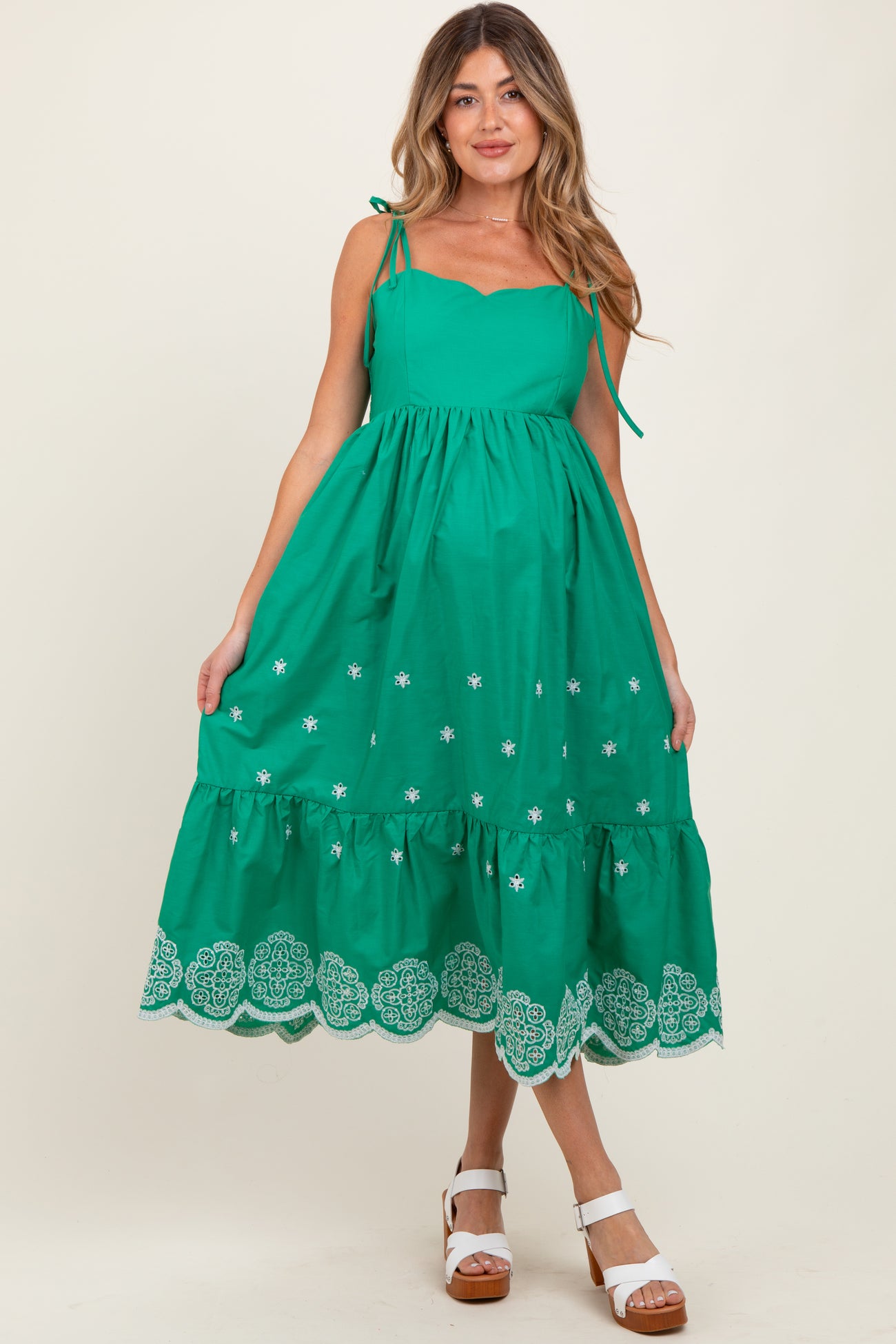 woman wearing a green sleeveless maternity dress with embroidered details and a tiered hem, showing her baby bump