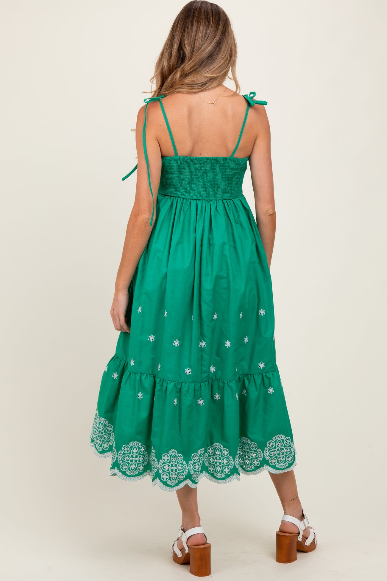 woman wearing a green maternity sundress with adjustable straps and lace detailing on the hem