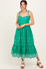 woman wearing a green sleeveless maxi dress with adjustable straps and embroidery details at the hem