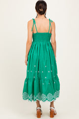 woman wearing a green midi dress with adjustable straps and embroidered details, showing the back view