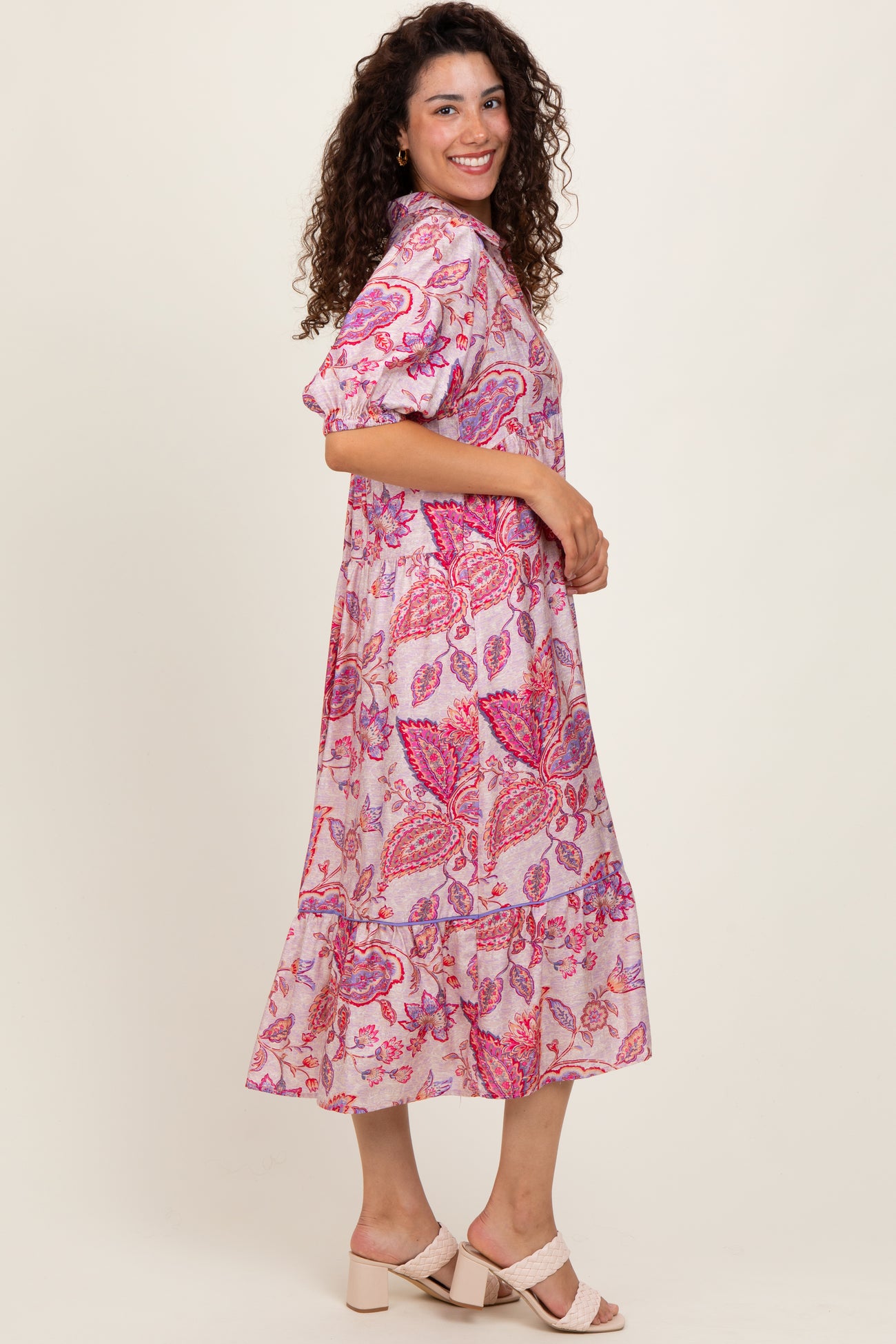 woman wearing a pink paisley print midi dress with puff sleeves and a tiered hemline