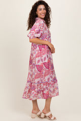 woman wearing a pink paisley print midi dress with puff sleeves and a tiered hemline