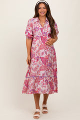 woman wearing a pink floral maternity dress with short puff sleeves and a tiered skirt, holding her baby bump